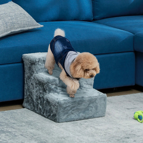 Perro pequeño bajando una escalera gris de tres peldaños junto a un sofá